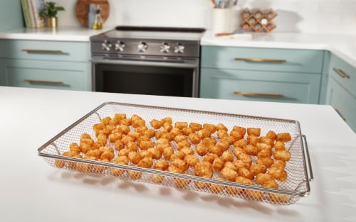 Tater tots in an air fry basket on a kitchen island