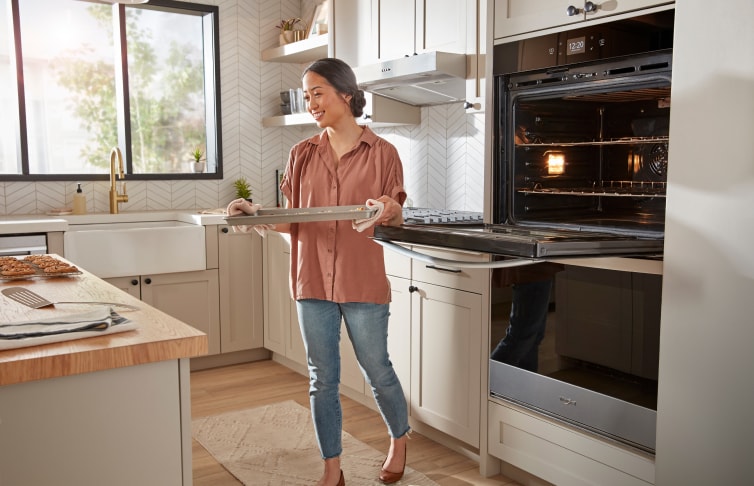 A person removing a tray of food from a Whirlpool® Wall Oven