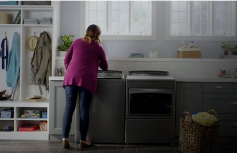 A person interacting with a Whirlpool® Top Load Washer and Dryer in a laundry room