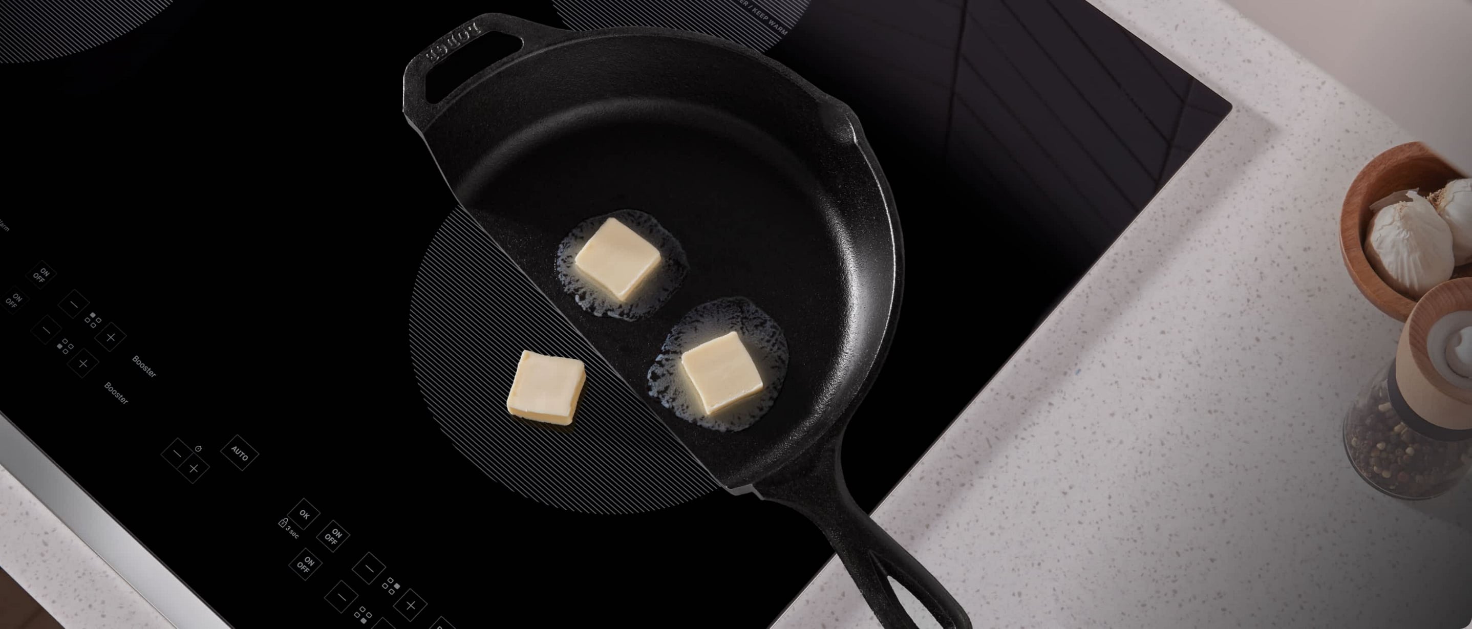 A frying pan cut in half on an induction cooktop, showing butter melting in the pan and not melting on the exposed element.