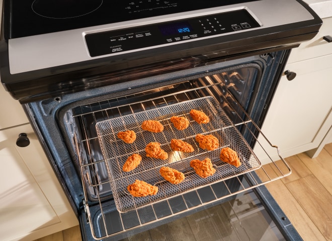 A basket of chicken wings being air fryed in an oven