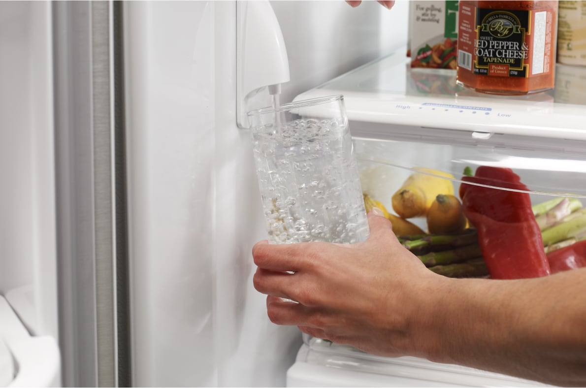 Filling a water glass from a refrigerator water dispenser.