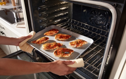 Person pulling spiced chicken breasts from an oven