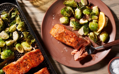 A closeup of air fried salmon on a plate with Brussel sprouts.