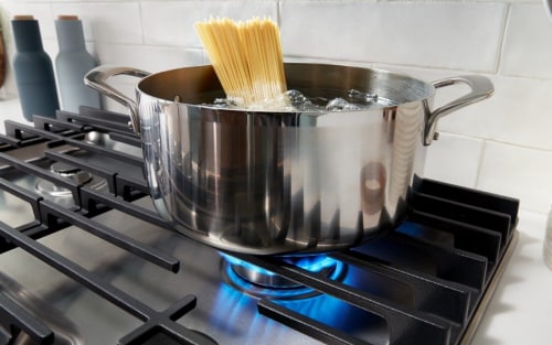 A pot resting on gas stove burner grates.