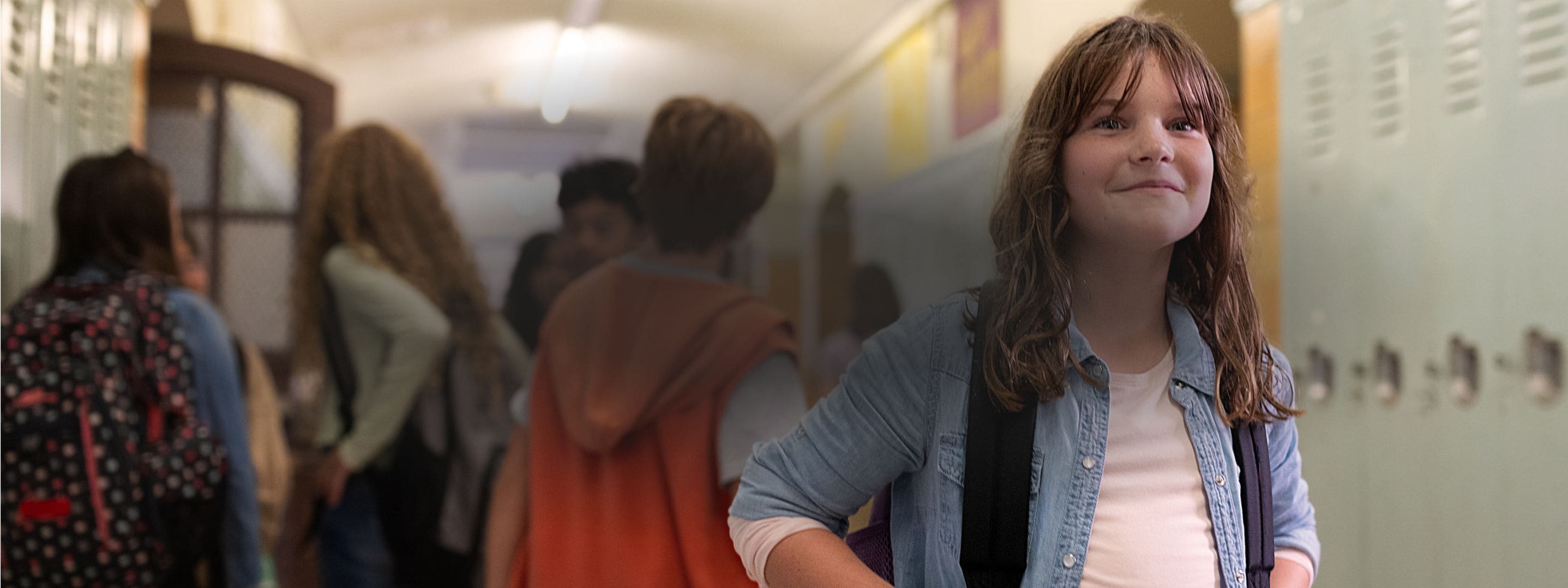 A smiling child in a school hallway with other kids behind them