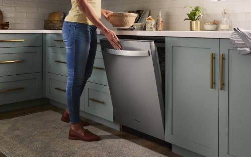 A closeup of a person opening a Whirlpool® dishwasher.