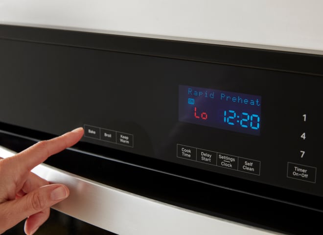 Closeup of a Whirlpool® Wall Oven console showing Rapid Preheat and a hand pressing the Bake button