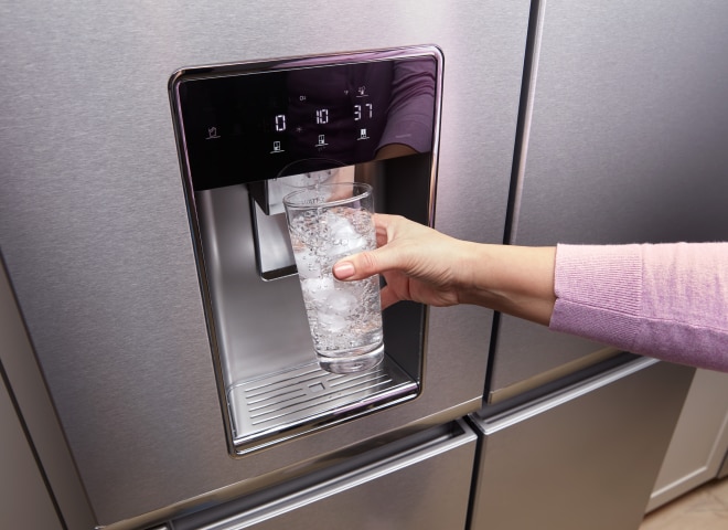 A hand getting water from the fridge dispenser