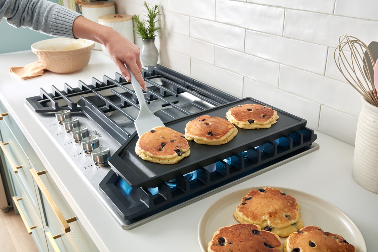 A person cooking pancakes on the griddle.