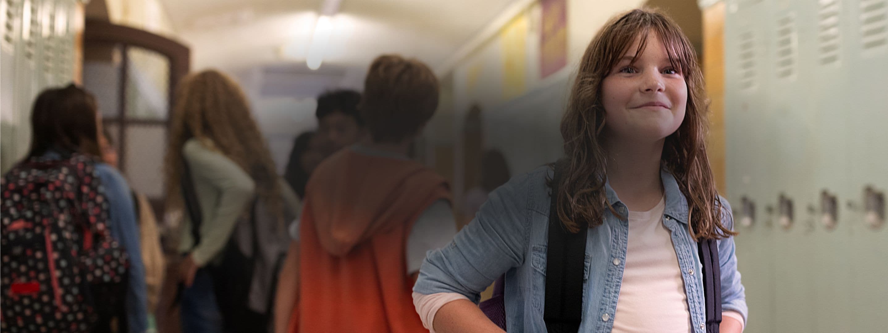  A smiling child in a school hallway with other kids behind them