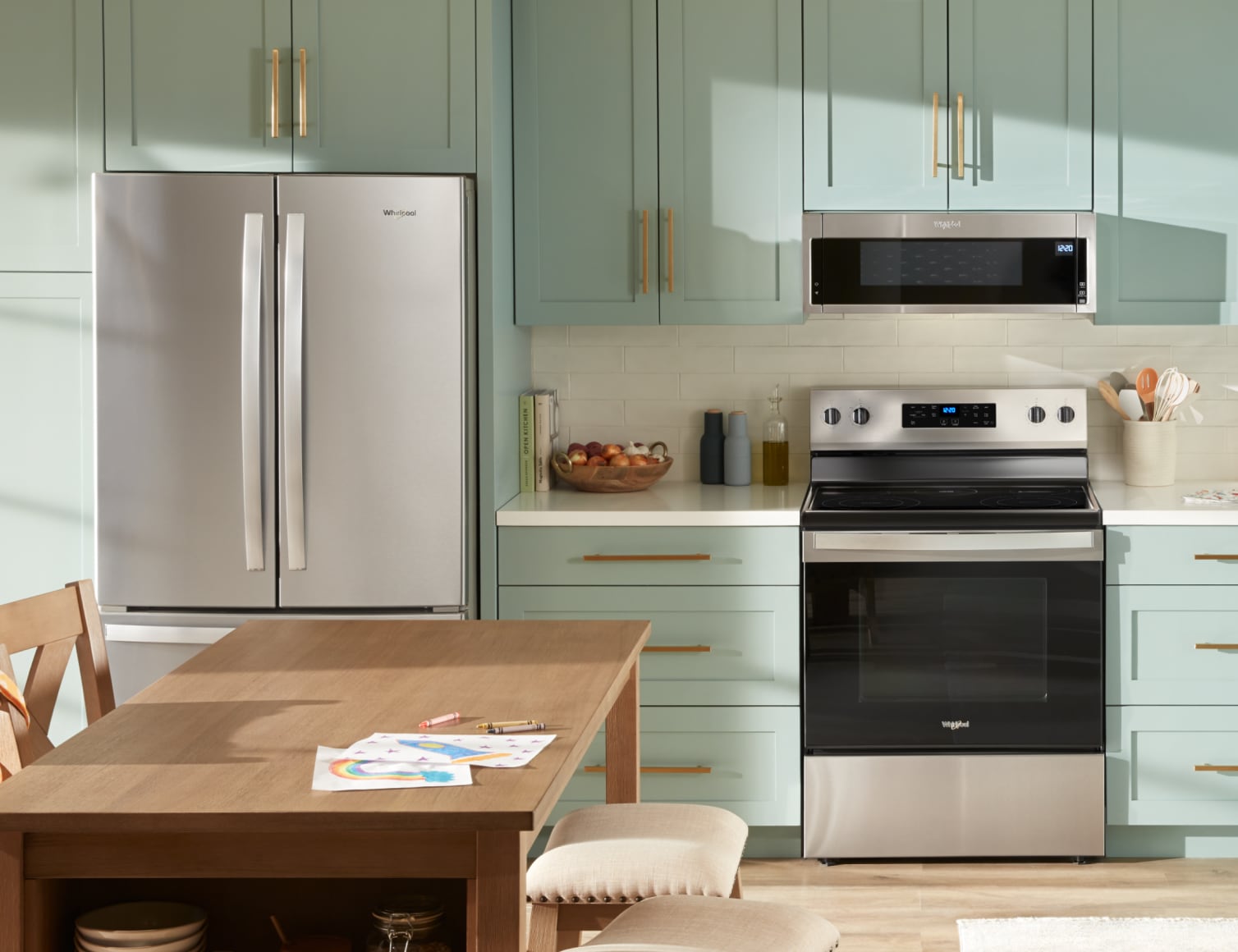 A suite of Whirlpool® appliances in a kitchen with light green cabinets and a wood kitchen island