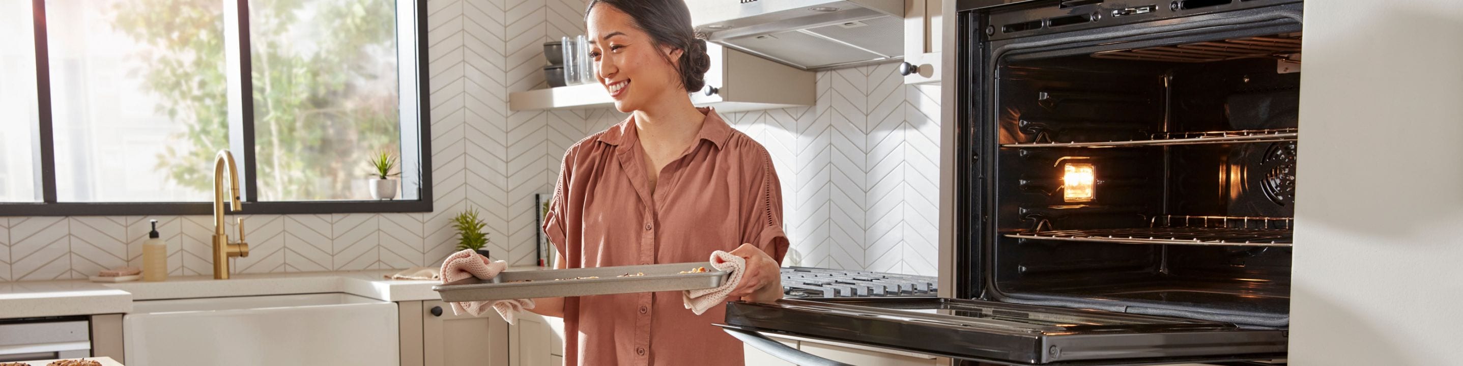 A person removing a tray of food from a Whirlpool® Wall Oven 