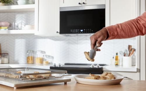 Person removing food from air fry basket with tongs