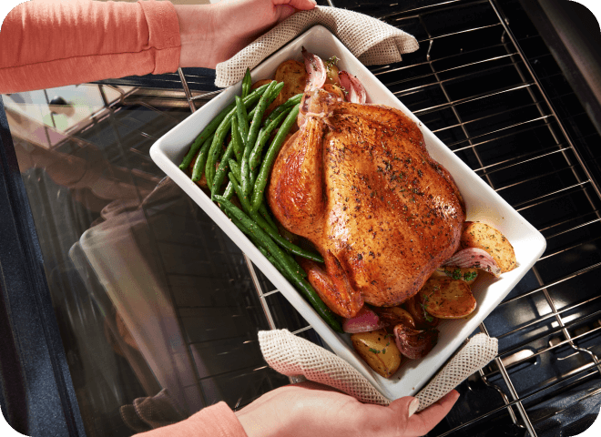 Person pulling a roasted chicken and vegetables out of a Whirlpool® Range