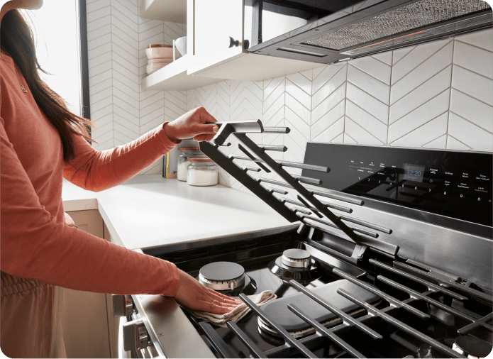 Hands wiping up underneath the EZ-2-Lift™ Hinged Cast-Iron Grates on a Whirlpool® Range