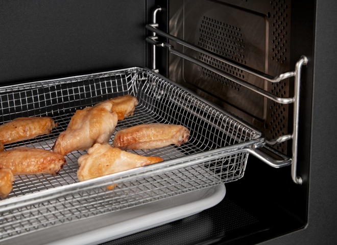 The inside of a microwave with chicken wings in the air fry basket.