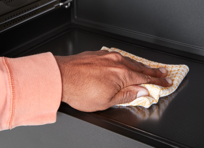 A person wipes the inside of a microwave with a cloth.